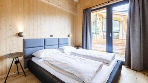 Ein modernes Schlafzimmer mit einem großen Bett, Holzwänden und Blick auf eine Holzterrasse.