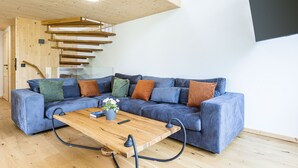 Ein modernes Wohnzimmer mit einem blauen Ecksofa, einem Holztisch und einer Treppe mit Holzbalken.