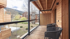 Un ponteggiato in legno con ringhiera in vetro, due poltrone in vimini e vista su un paesaggio montuoso.