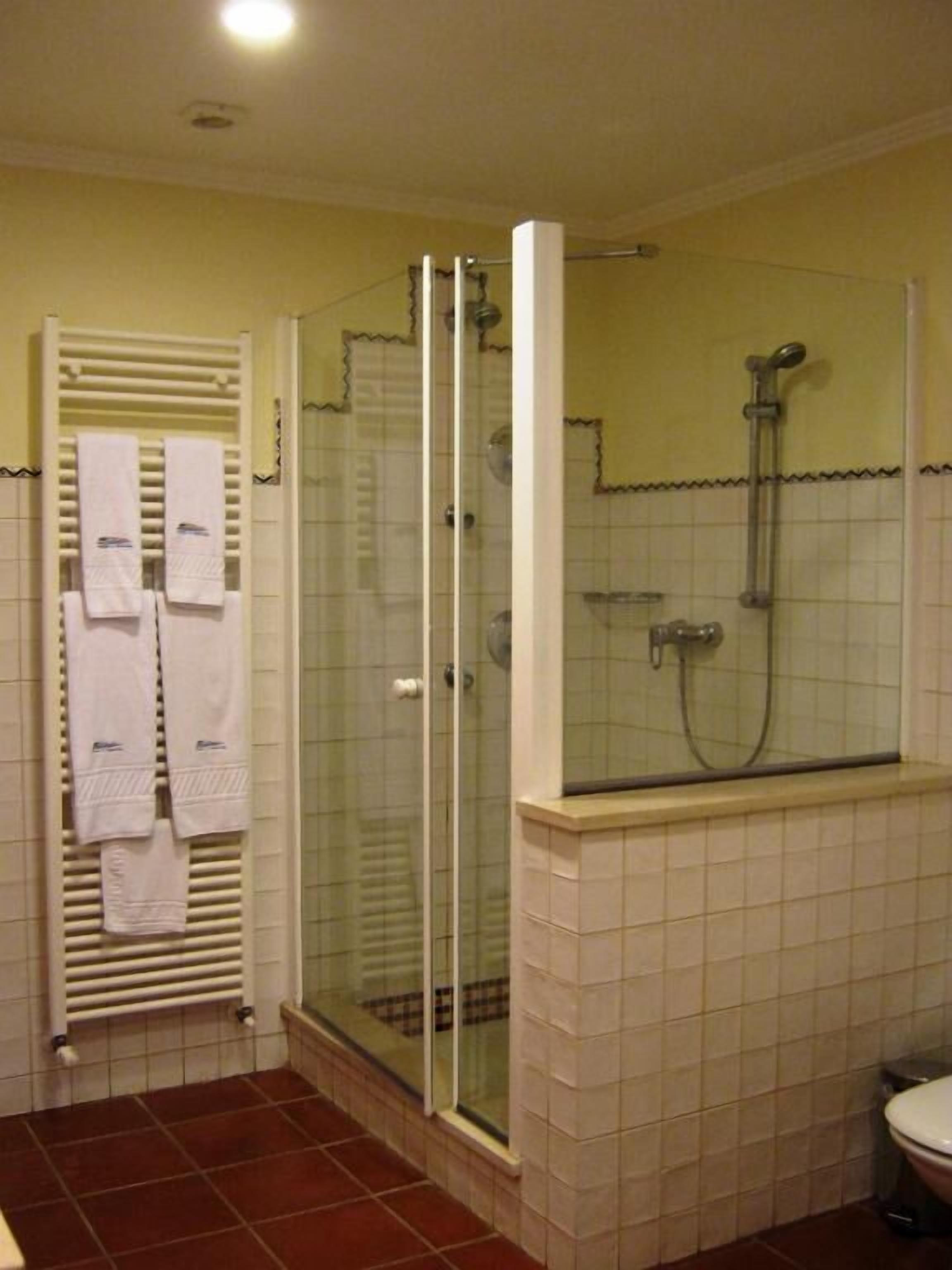 A bathroom with a glass-enclosed shower, a toilet, and a towel rack with towels.