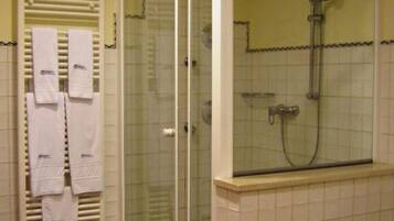 A bathroom with a glass-enclosed shower, a toilet, and a towel rack with towels.