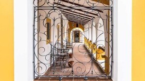 Une vue encadrée d’un couloir avec une porte en fer forgé, un sol carrelé et un banc.