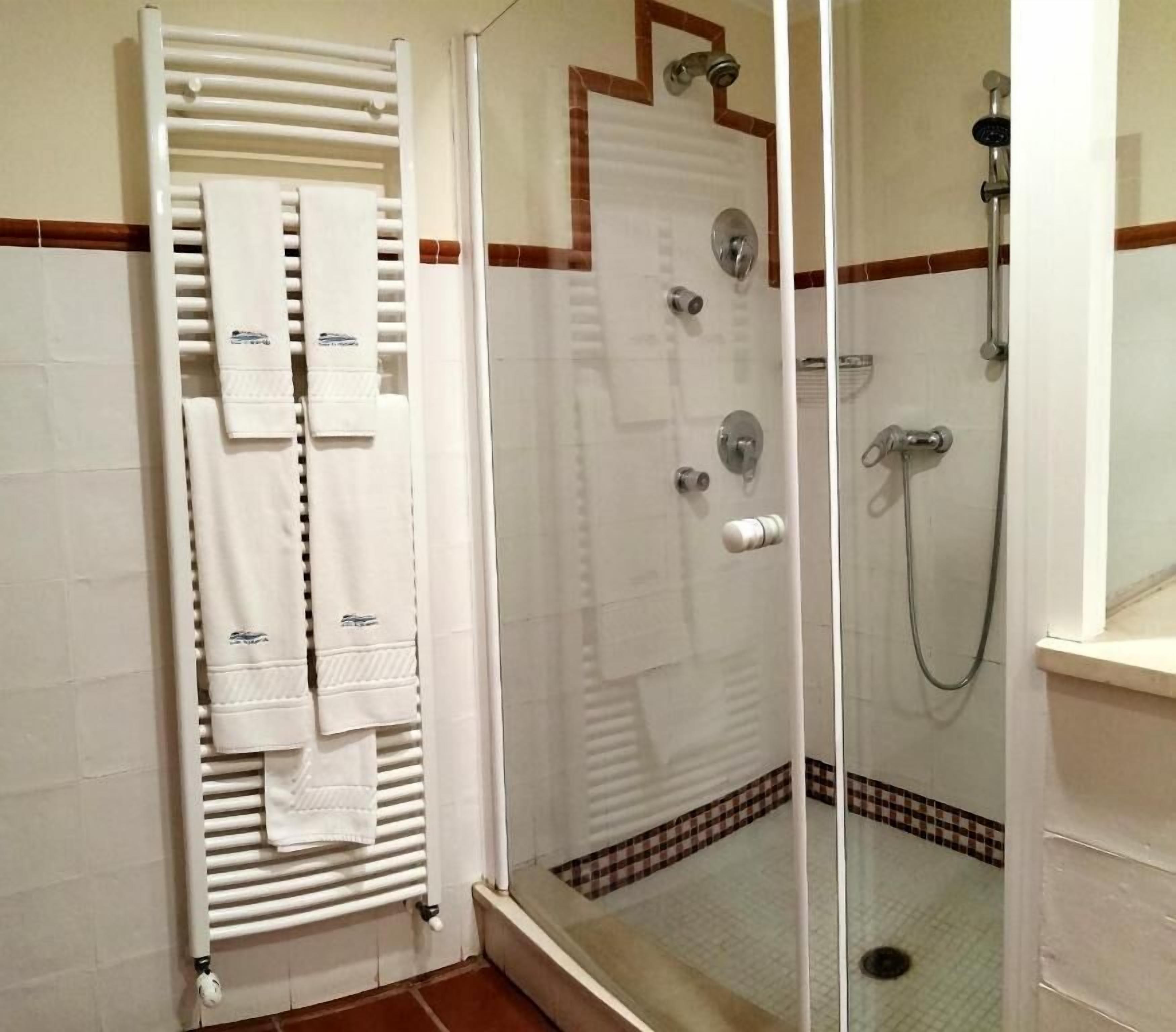 Un espacio de ducha con puerta de vidrio, un perchero con varias toallas y un cabezal de ducha.