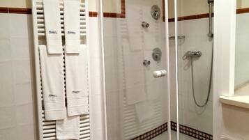 Un espacio de ducha con puerta de vidrio, un perchero con varias toallas y un cabezal de ducha.