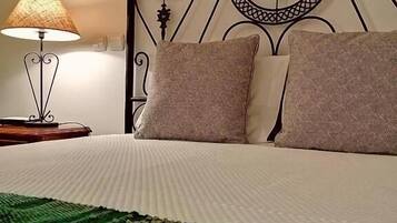 A neatly made bed with a patterned green blanket, a decorative metal headboard, and a bedside lamp.
