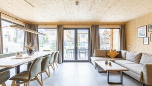 Un interior moderno con techo de madera, un comedor con sillas y una mesa, un sofá y un amplio ventanal corredera que da a un patio exterior.