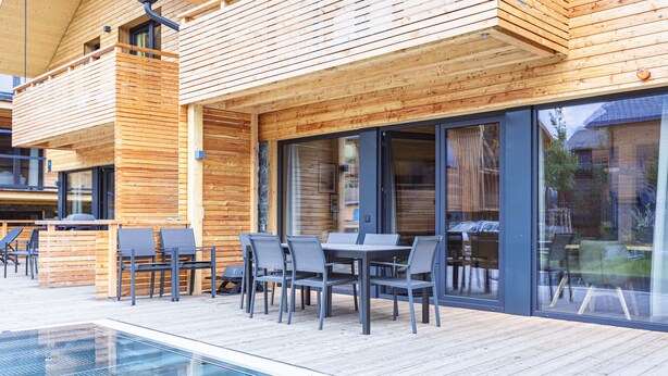 Una terraza de madera con piscina, mobiliario exterior y grandes ventanales.