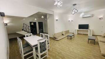 A modern living room with a dining area, a sofa, a TV, and a staircase leading to another level.