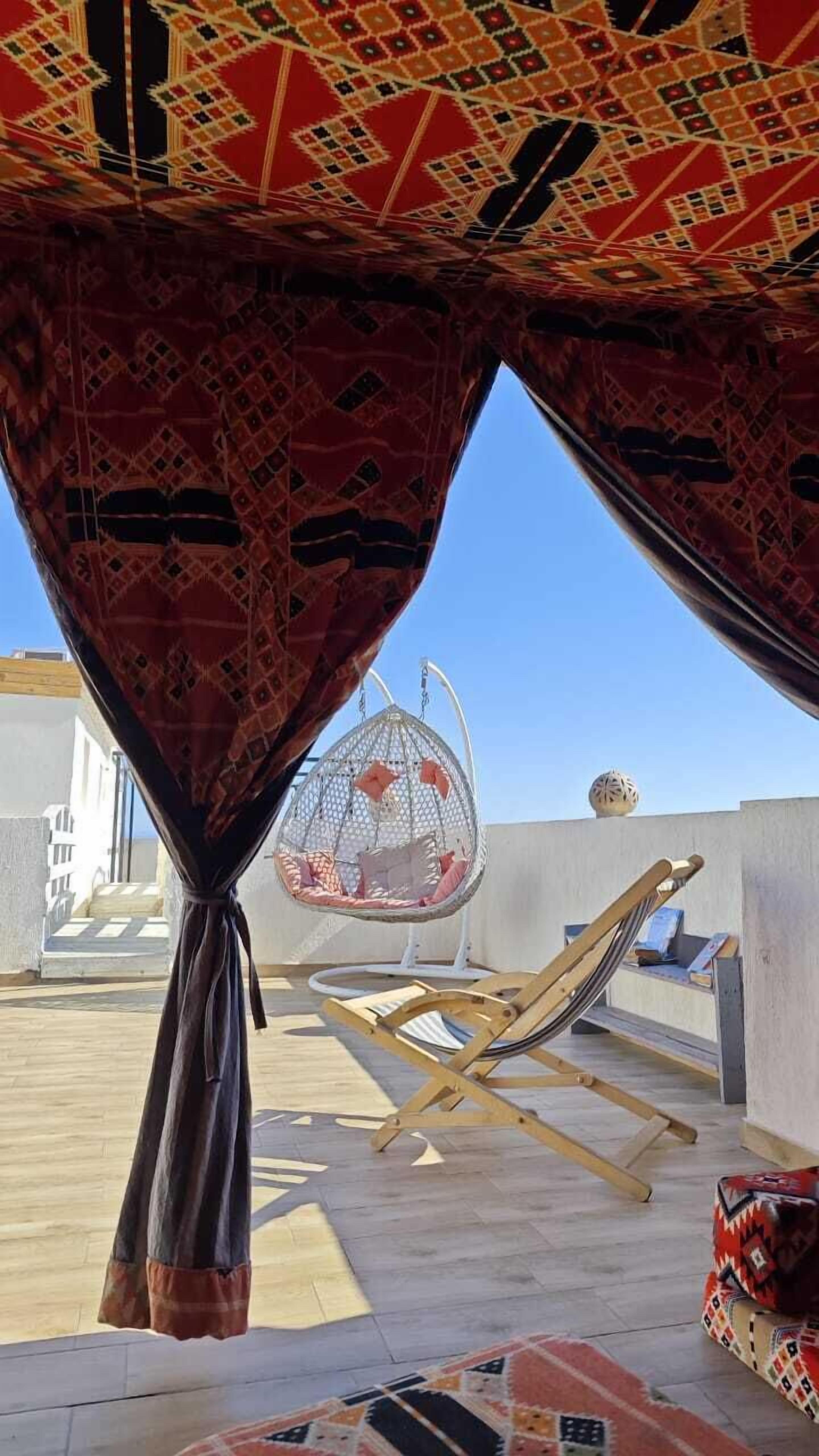 Un espace extérieur aménagé avec des sièges, protégé par un auvent à motifs, comprenant un fauteuil suspendu et un hamac.