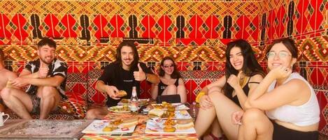 A group of people sitting around a table with various dishes, in a room with patterned walls and a traditional design.
