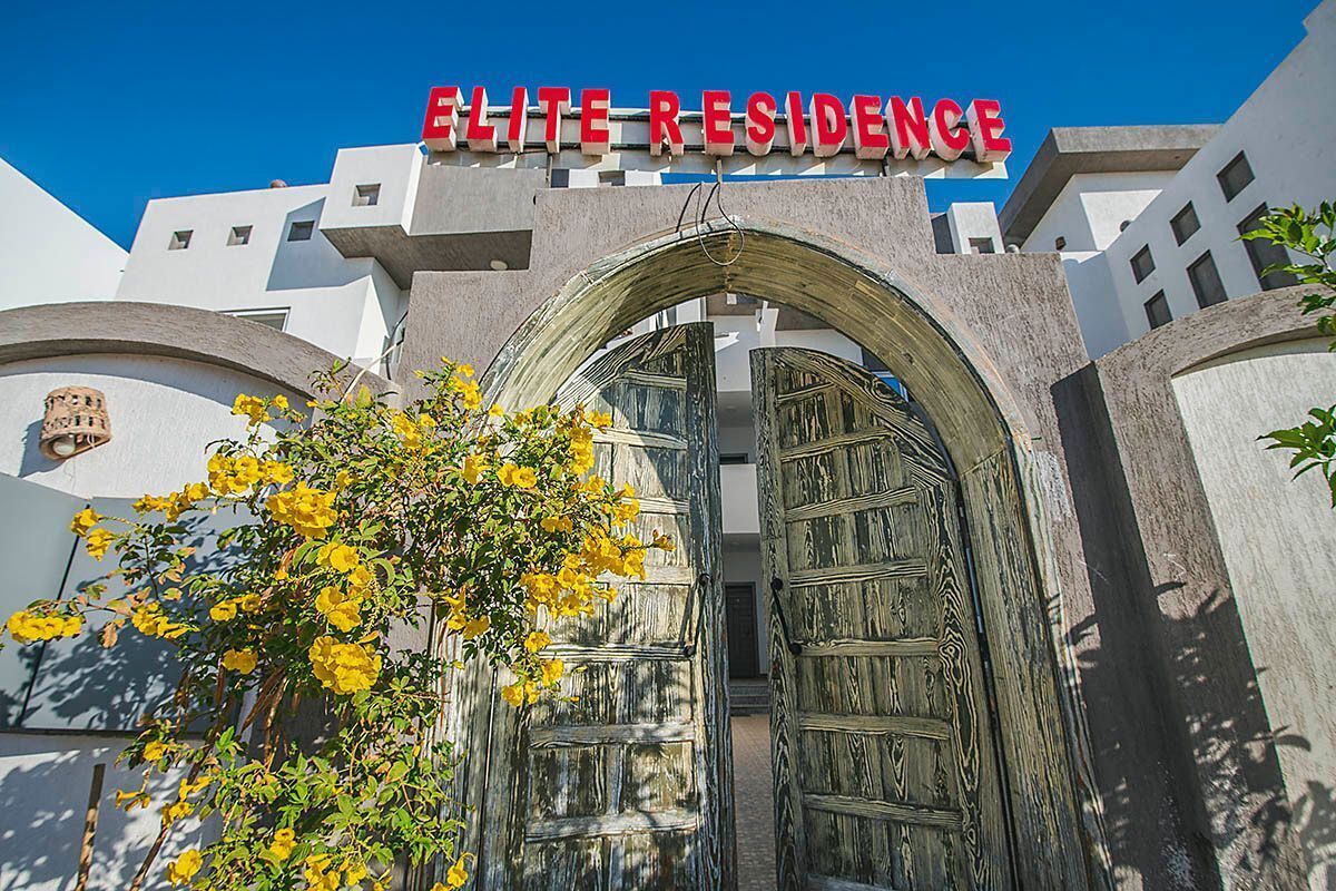 Entrada de un edificio con un letrero que dice "ELITE RESIDENCE" y una puerta de madera grande.