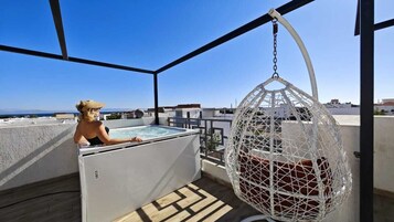 Una terraza en la azotea con un jacuzzi, una silla colgante y vistas al mar.