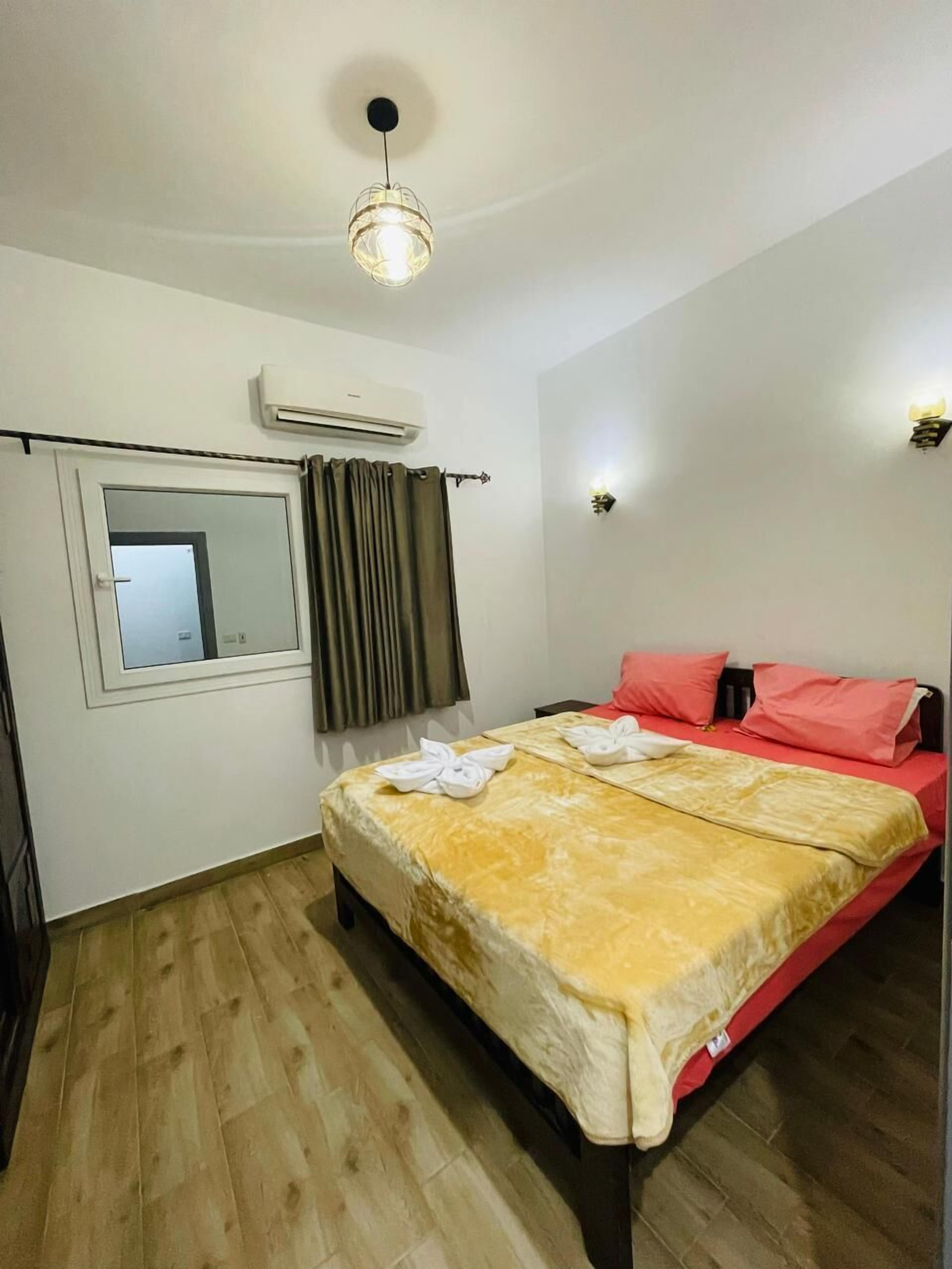 A bedroom with a bed, a window with curtains, an air conditioning unit, and a light fixture.