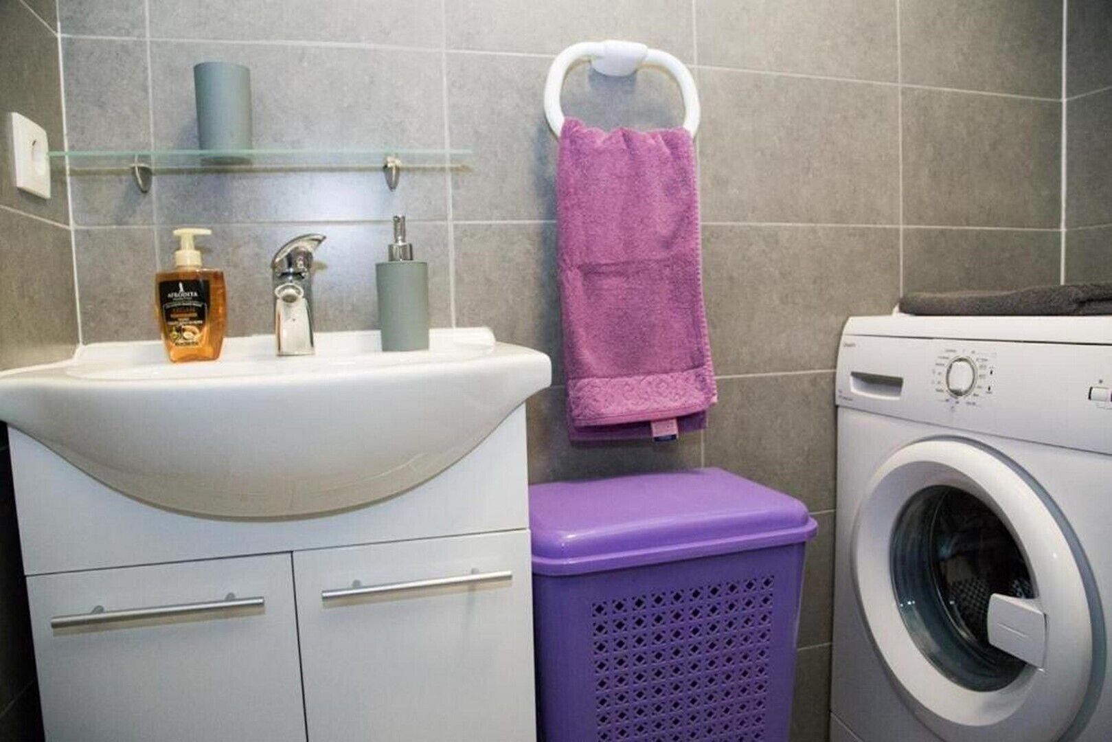 Ein Badezimmer mit einem weißen Waschbecken, einem violetten Wäschekorb und einer Waschmaschine.