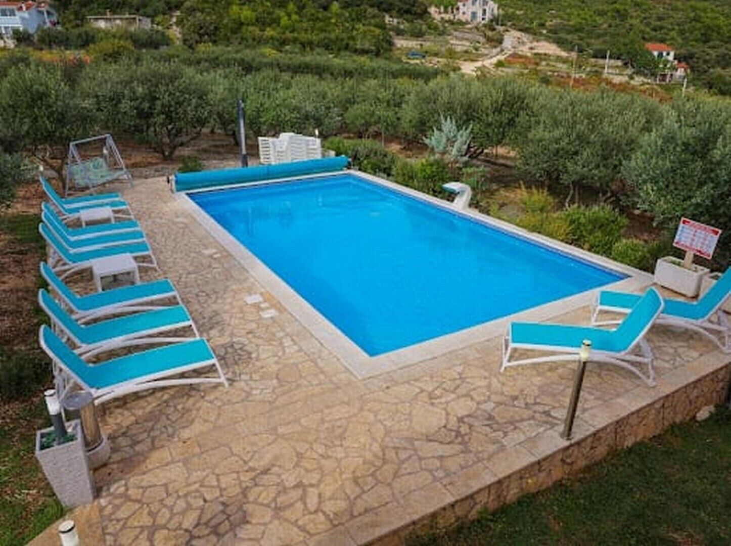 Ein rechteckiger Pool mit blauem Wasser, umgeben von Steinplatten und blauen Liegestühlen.
