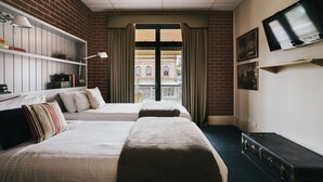Camera d'albergo con due letti, una televisione, una libreria e vista su un edificio.