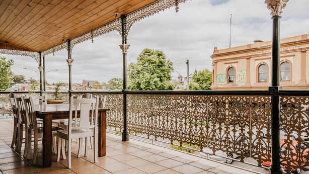 Un'area pranzo all'aperto riparata, con tetto in legno e elaborate ringhiere in metallo, con vista su una città che presenta edifici storici.