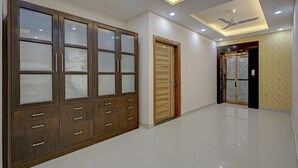 Um corredor amplo com um guarda-roupa de madeira grande, uma porta de madeira e um ventilador de teto.