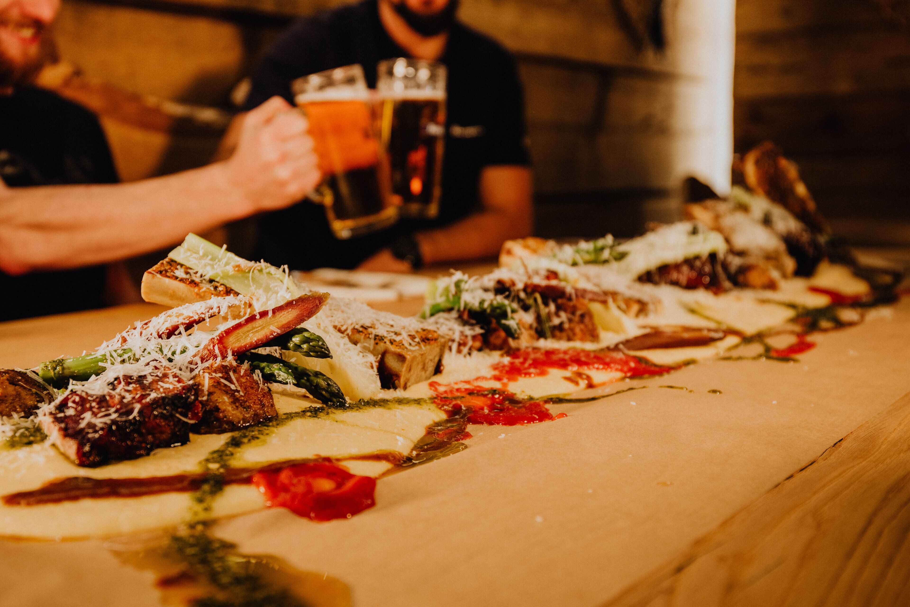 A long table with various dishes, including pizzas and a beer glass.