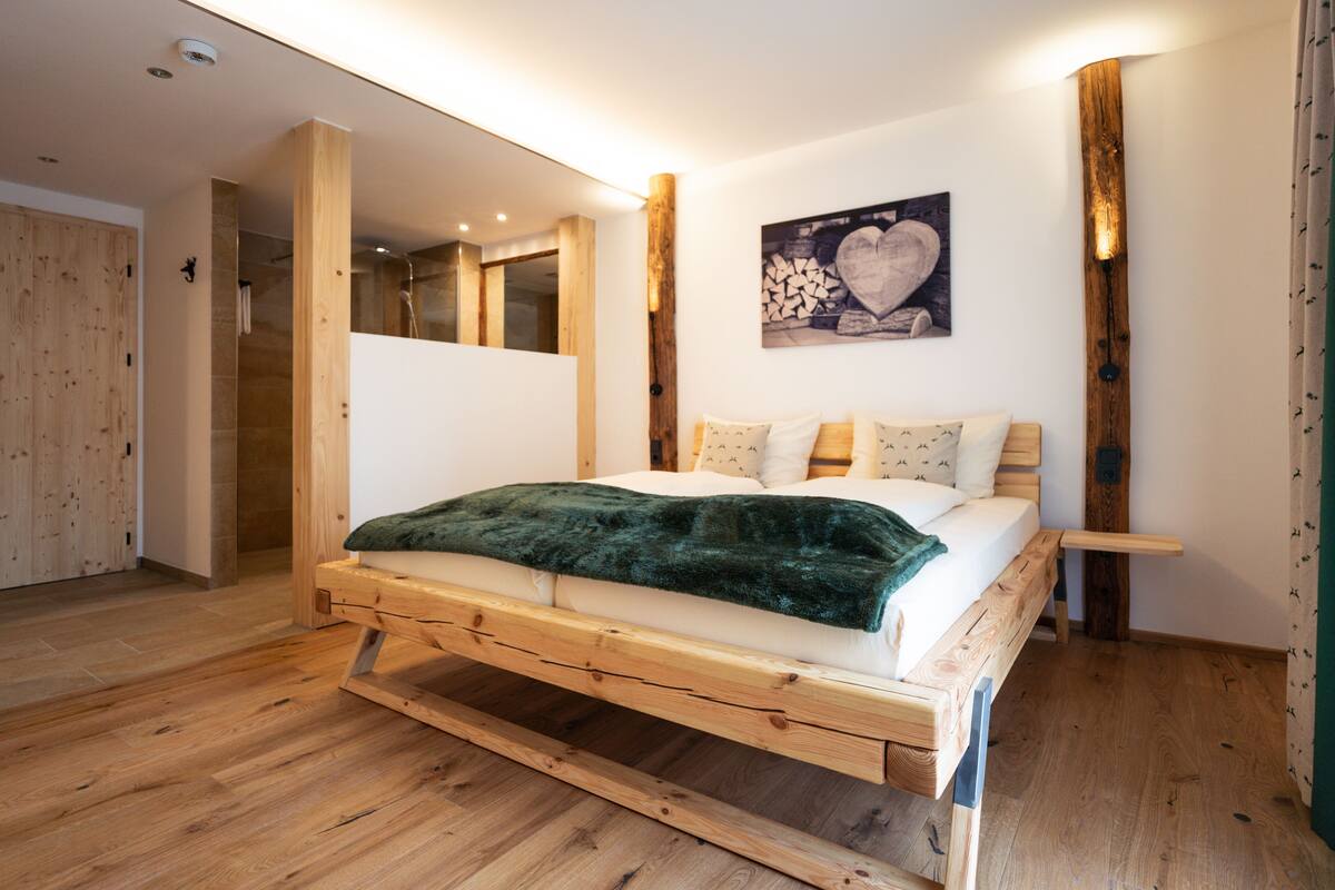 Uma cama de madeira com um cobertor verde, cabeceira de madeira e um quadro de coração fixado na parede.