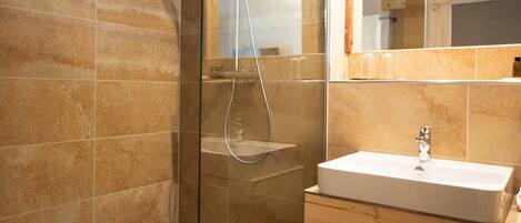 Un baño moderno con ducha envuelta en vidrio, tocador de madera y un espejo grande.