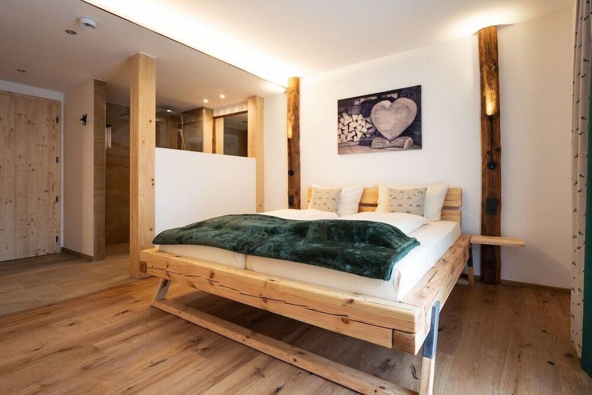 Uma cama de madeira com um cobertor verde, um banco de madeira e um quadro pendurado na parede.