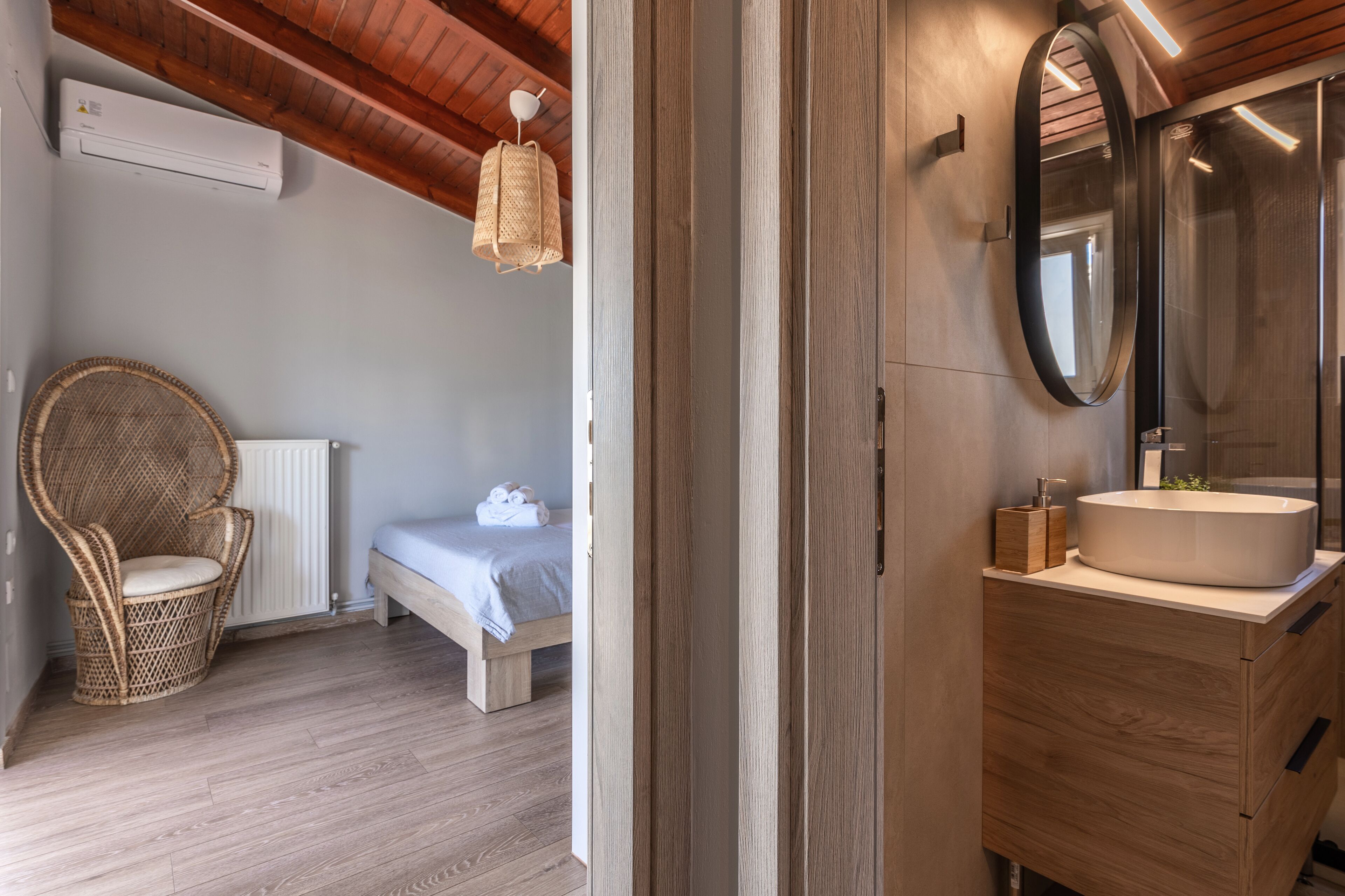 A bedroom with a bed, a wicker chair, a bedside table, and a large mirror.