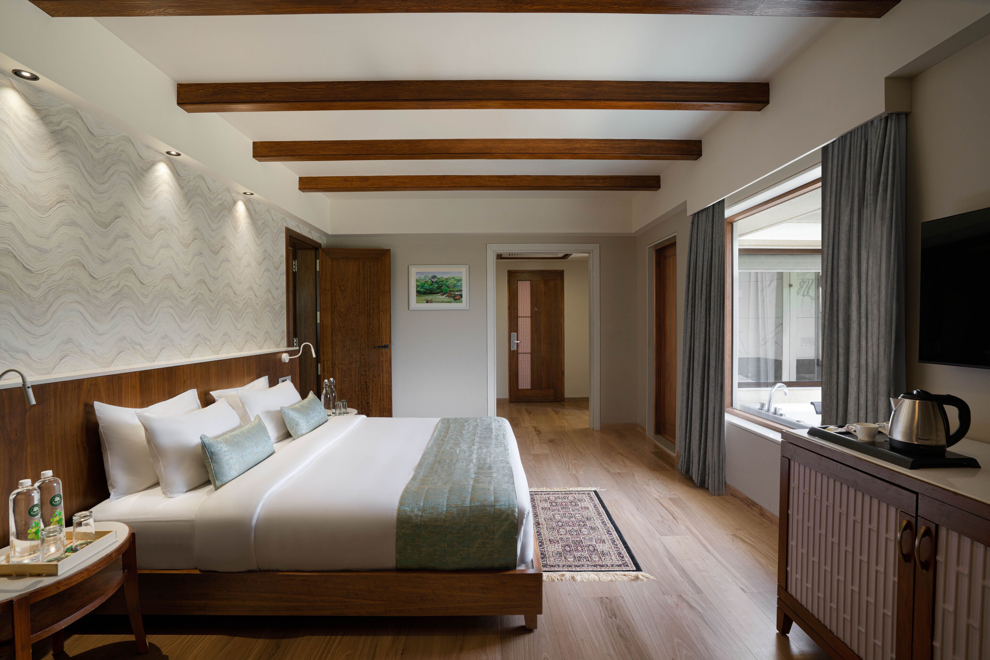 A modern hotel room with a large bed, wooden headboard, a flat-screen TV, and a window with curtains.