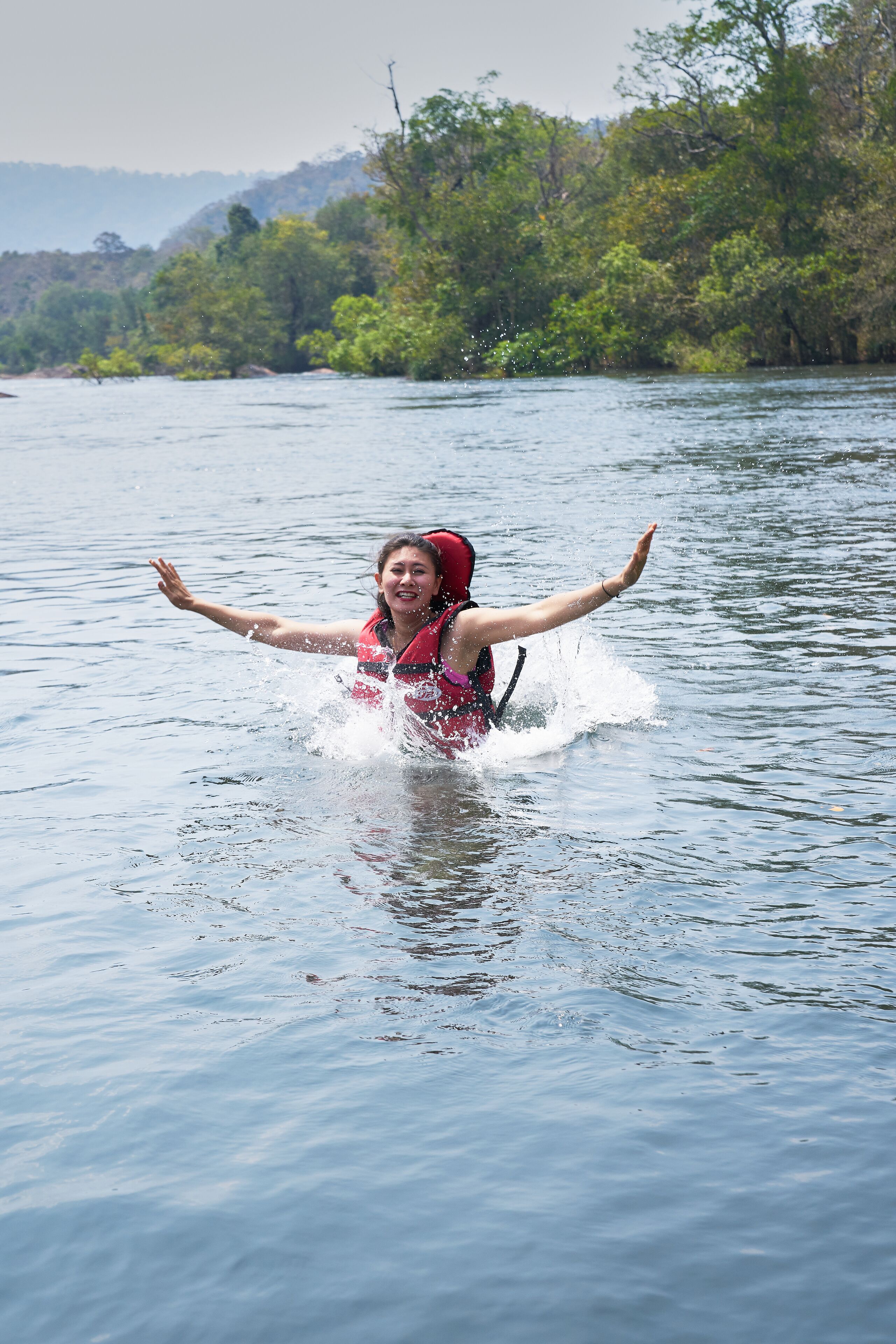 Eine Person im roten Schwimmwesten planscht im Wasser, im Hintergrund Bäume.