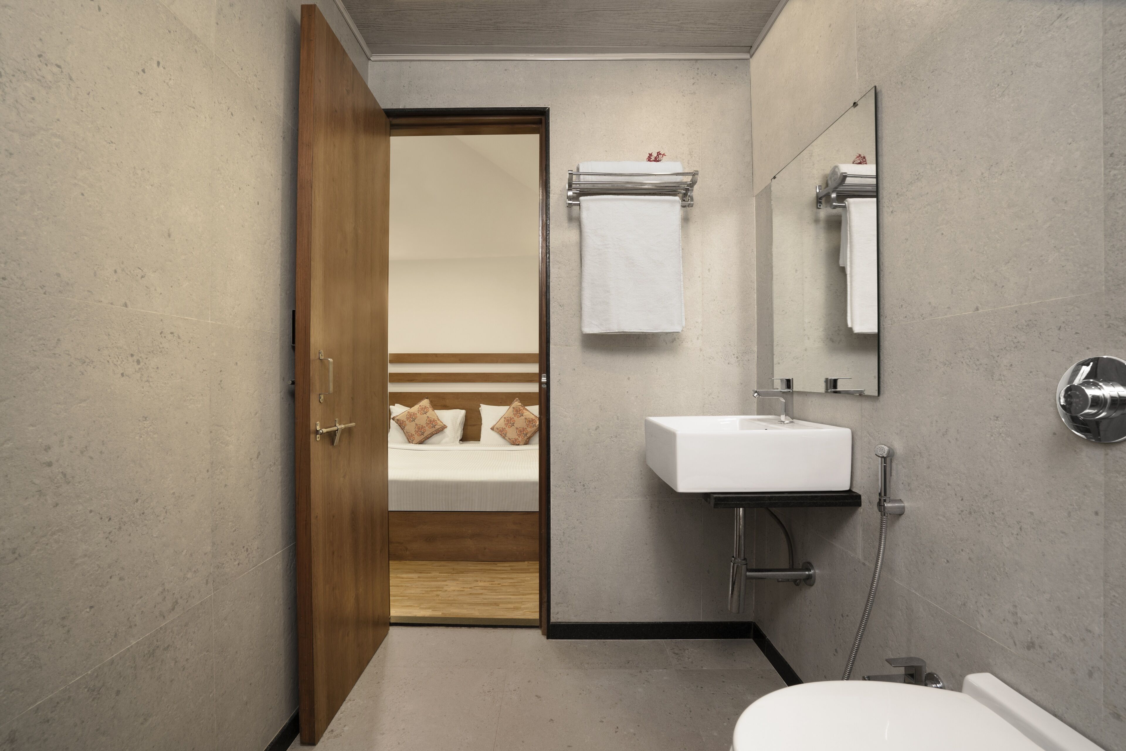 A modern bathroom with a wooden door, a white sink, a mirror, and a toilet.
