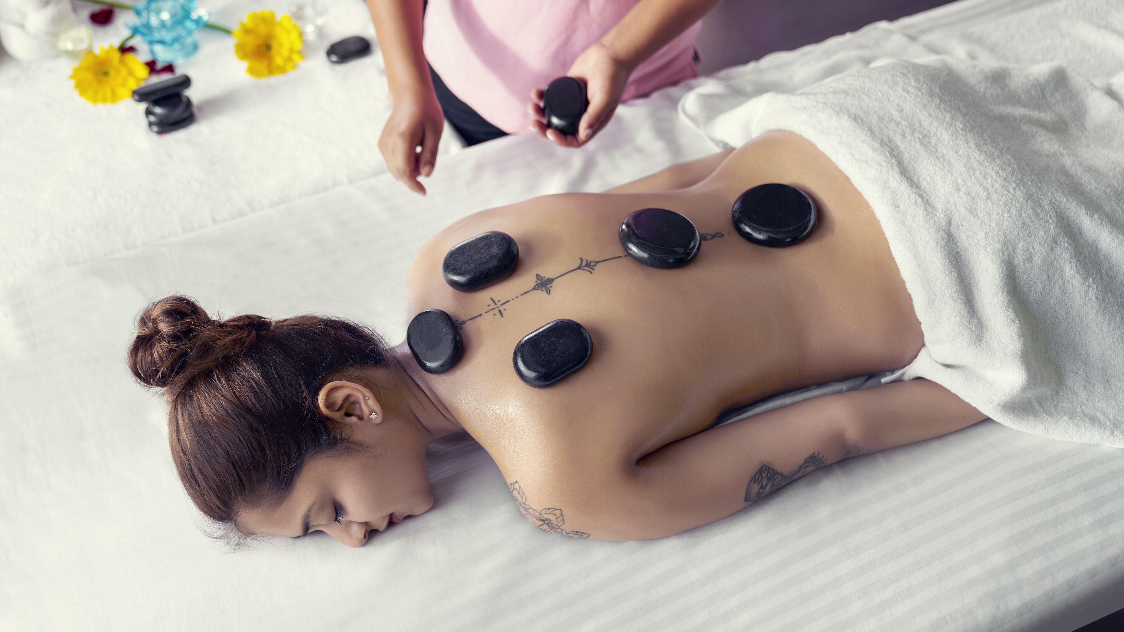 A person receiving a back treatment with stones on their back, lying on a bed with a white sheet.