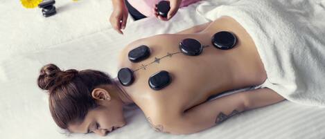A person receiving a back treatment with stones on their back, lying on a bed with a white sheet.