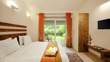 Habitación de hotel con una cama grande, cabecera de madera, televisor de pantalla plana, un banco con un florero y vistas a zonas verdes por la ventana.