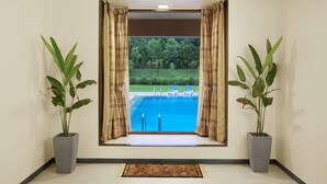 Habitación con un ventanal grande que da a una piscina y un jardín. Hay dos plantas en macetas a cada lado de la ventana.