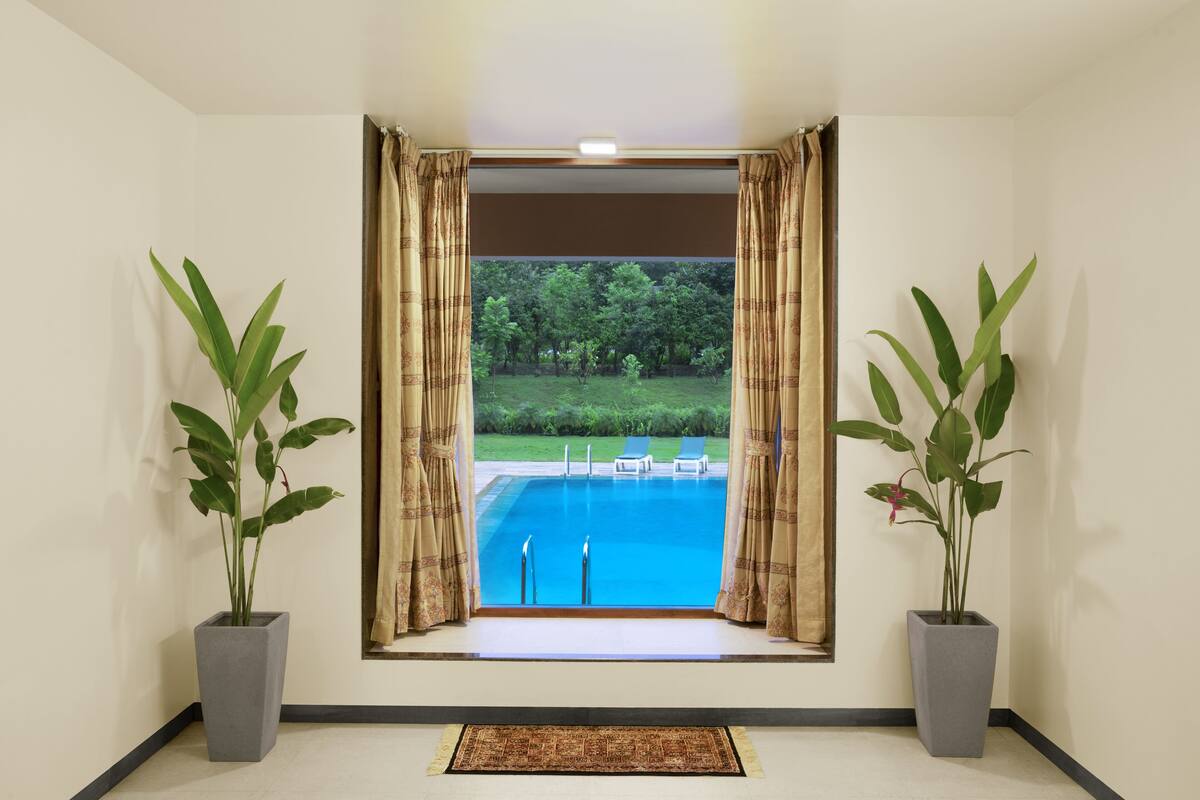 Et værelse med et stort vindue, der kigger ud over en swimmingpool og have. Der er to krukker med planter på hver side af vinduet.
