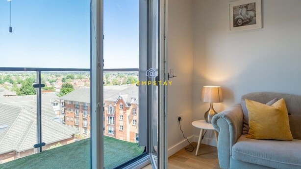 A room with a large window, a sofa, a lamp, and a framed picture on the wall. - 1BR Apt Near Heathrow By Tempstay (Slough)