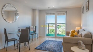 A modern living room with a glass dining table, a sofa, and a large mirror. - 1BR Apt Near Heathrow By Tempstay (Slough)
