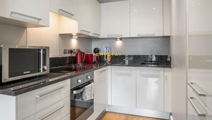 A modern kitchen with white cabinets, a black countertop, a microwave, a coffee maker, and a toaster. - 1BR Apt Near Heathrow By Tempstay (Slough)