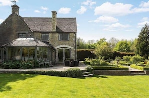 Une maison en pierre avec une véranda, une pelouse bien entretenue et un jardin agrémenté de haies.
