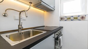 A modern kitchen with a stainless steel sink, a built-in oven, and a range hood. - Charming Studio in Graça Overlooking the Tagus River (Lisboa)