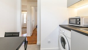 A compact kitchen with a microwave, washing machine, and a table with chairs. - Charming Studio in Graça Overlooking the Tagus River (Lisboa)