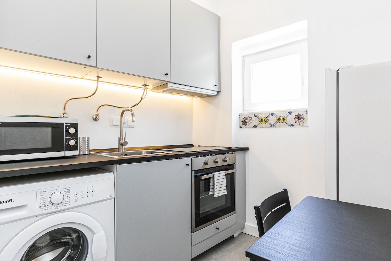 Una cucina compatta con forno a microonde, lavello, piano cottura e lavatrice.