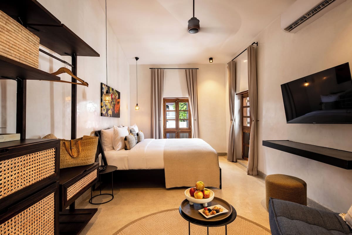 Una habitación de hotel moderna con cama, televisor montado en la pared, una mesita con fruta y un sofá.