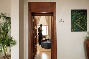 A hallway with a wooden door, a potted plant, a blue ottoman, and a painting on the wall. - The Neela Boutique Hotel Stone Town (Zanzibar Town)