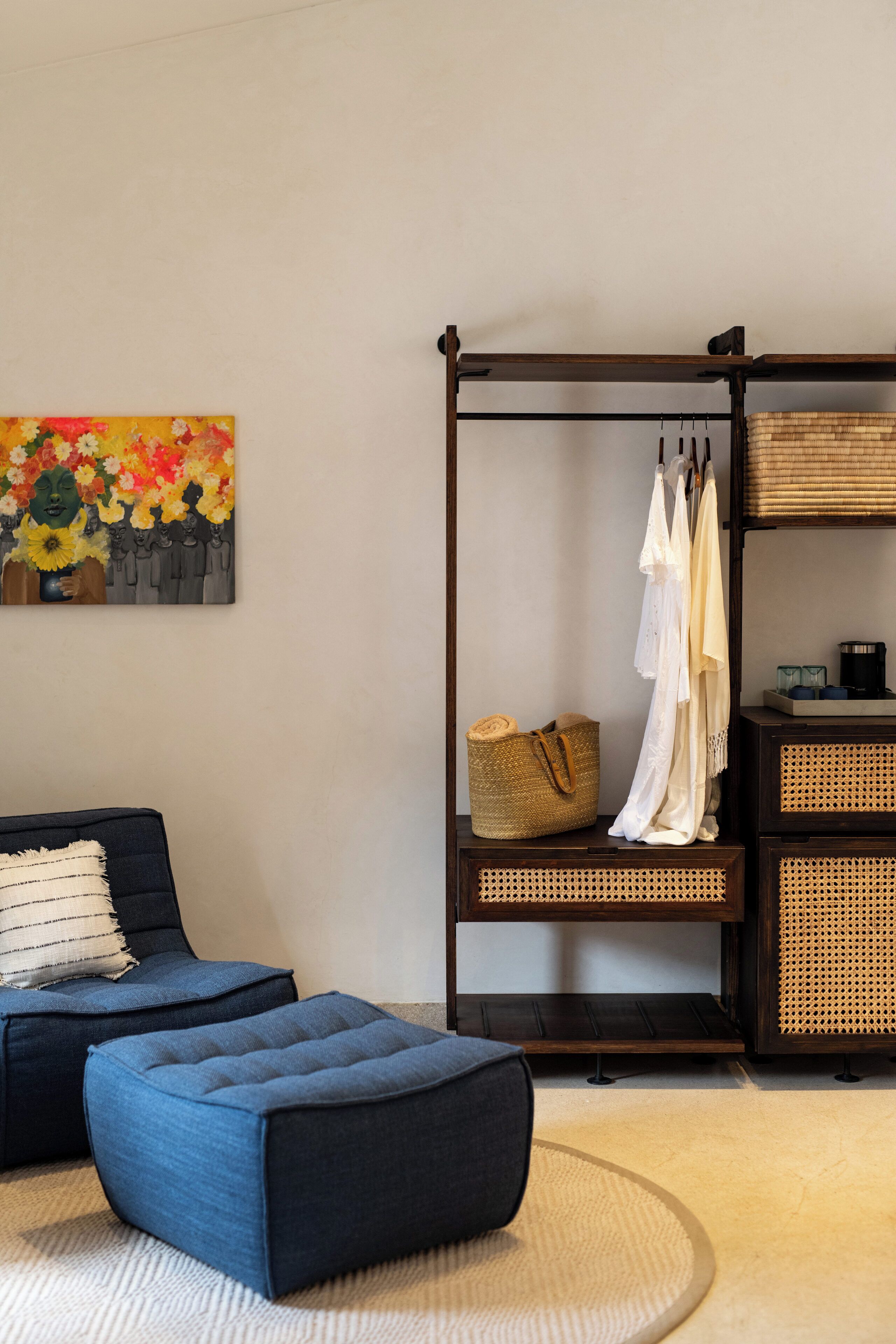 Una habitación con sofá, reposapiés, decoración en la pared, un perchero con ropa y cestas de almacenamiento.