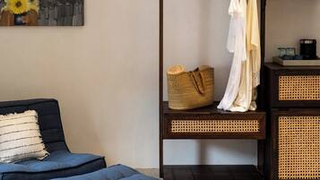 Una habitación con sofá, reposapiés, decoración en la pared, un perchero con ropa y cestas de almacenamiento.