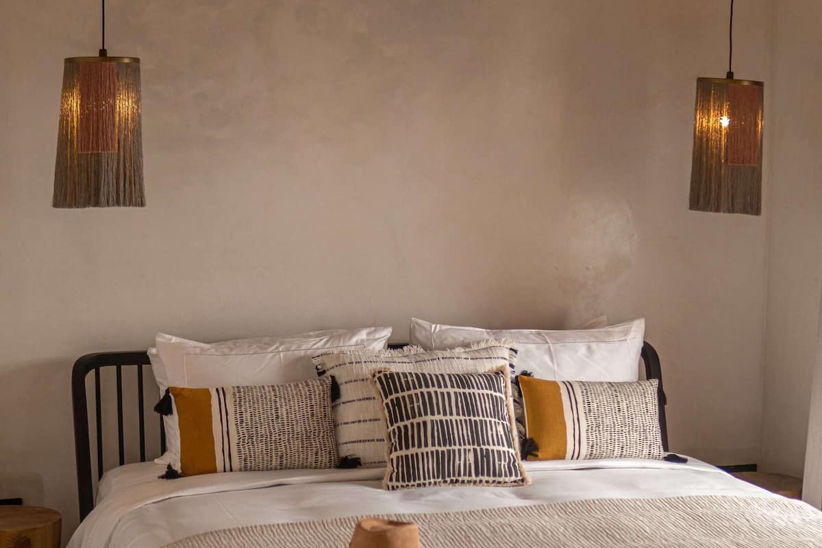 Una cama bien hecha con una variedad de almohadas y un sombrero rústico sobre la colcha.