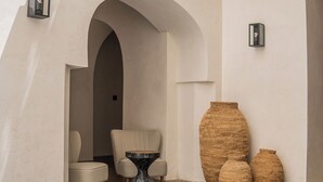 Un pasillo con un amplio arco de entrada, dos sillones tapizados, una mesa redonda y tres grandes jarrones tejidos.