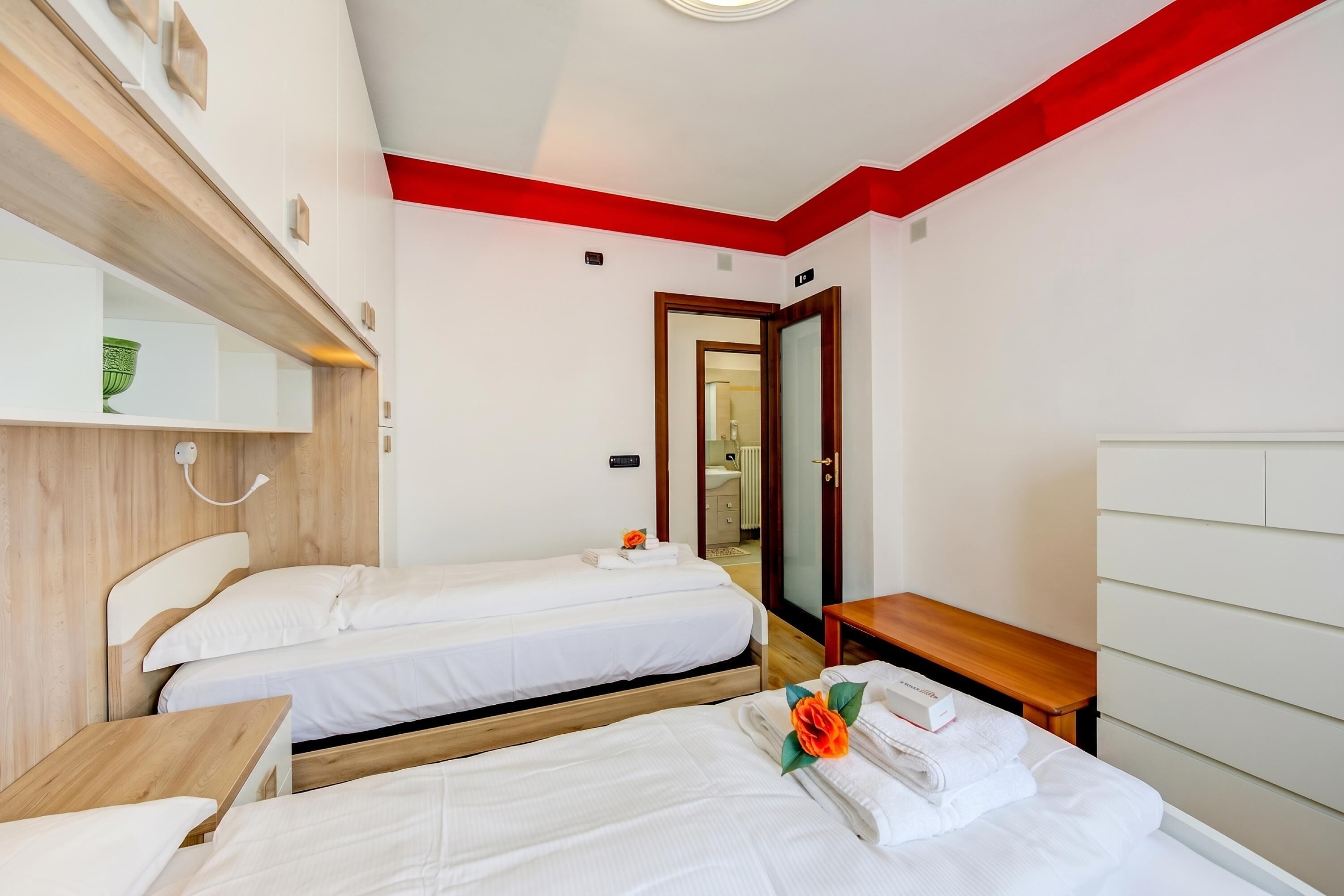Habitación de hotel con dos camas, un banco de madera, un espejo y una puerta que da a un baño.
