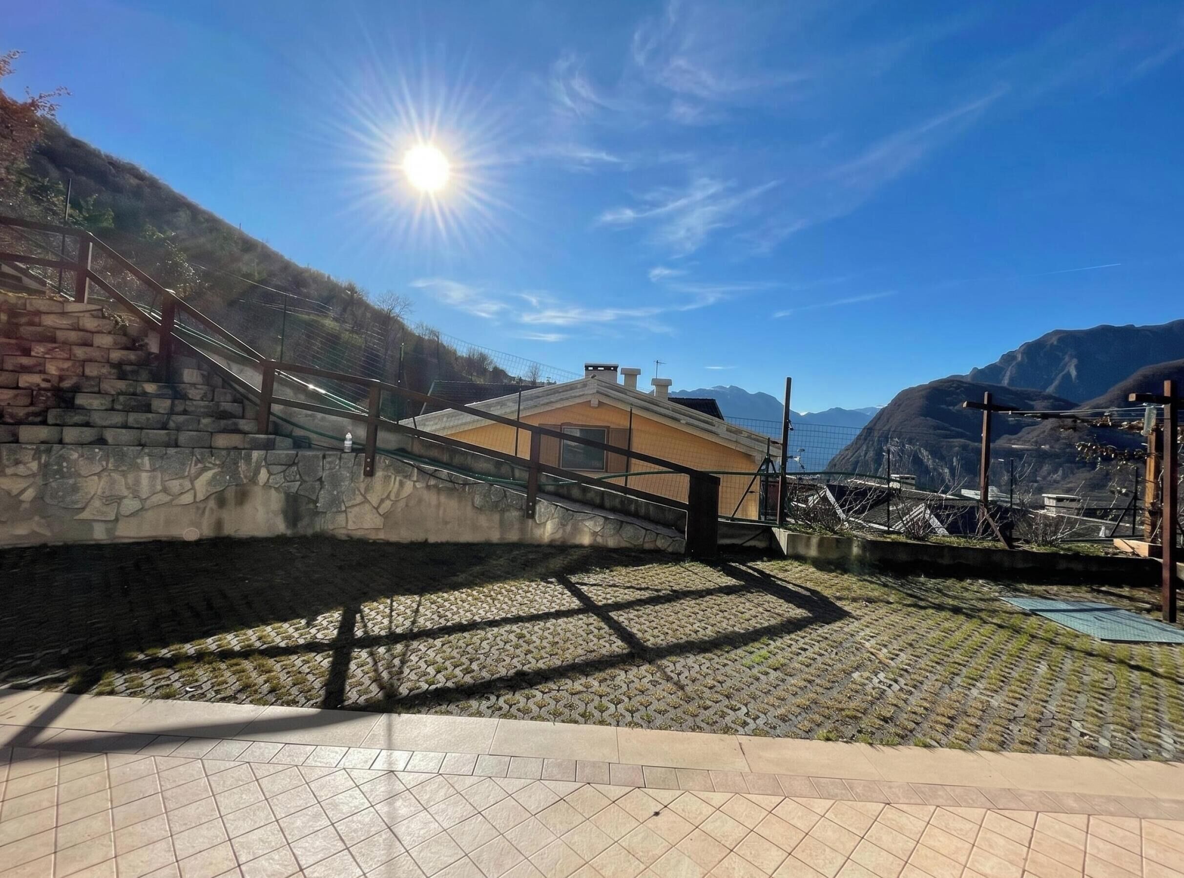 Un escalier menant à un bâtiment d’où l’on peut admirer des montagnes, un ciel dégagé et un soleil brillant.